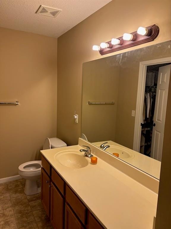 bathroom featuring a textured ceiling, toilet, baseboards, visible vents, and vanity