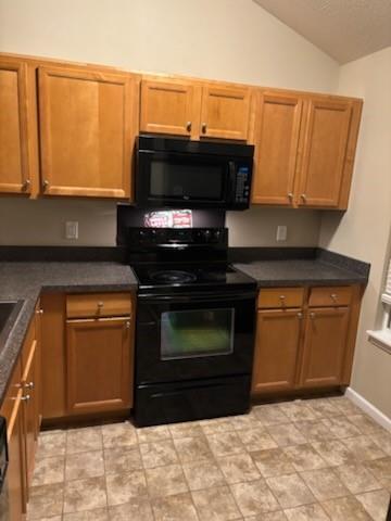 kitchen featuring dark countertops, black appliances, brown cabinets, baseboards, and lofted ceiling