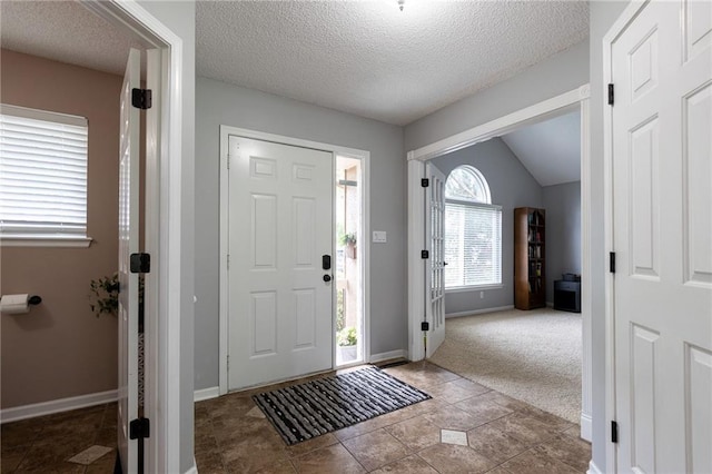 foyer featuring a textured ceiling, light carpet, baseboards, and lofted ceiling