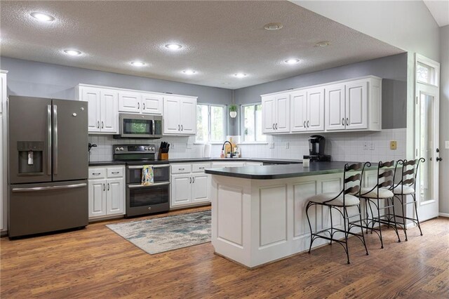 kitchen featuring a textured ceiling, dark countertops, appliances with stainless steel finishes, tasteful backsplash, and a peninsula