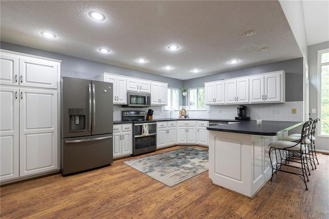 kitchen with stainless steel appliances, dark countertops, a textured ceiling, and a peninsula