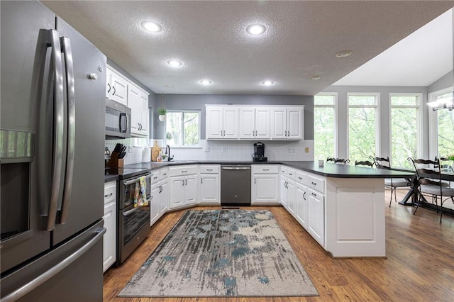 kitchen featuring a peninsula, dark countertops, a textured ceiling, tasteful backsplash, and appliances with stainless steel finishes