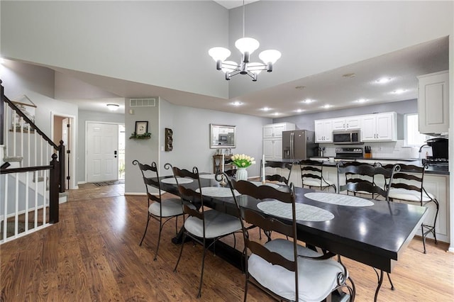 dining space featuring light wood-style floors, visible vents, an inviting chandelier, a high ceiling, and stairs
