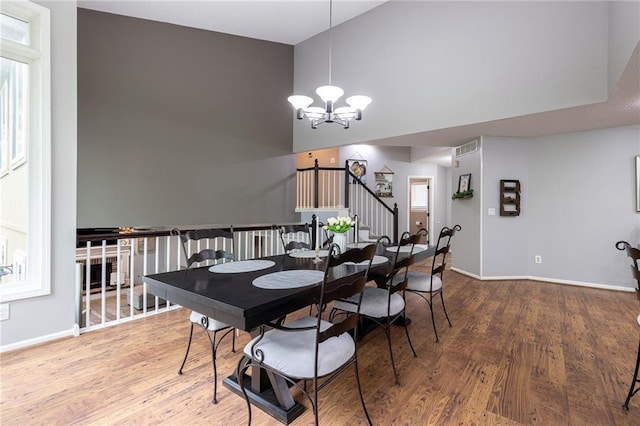 dining area featuring visible vents, a towering ceiling, wood finished floors, stairway, and an inviting chandelier