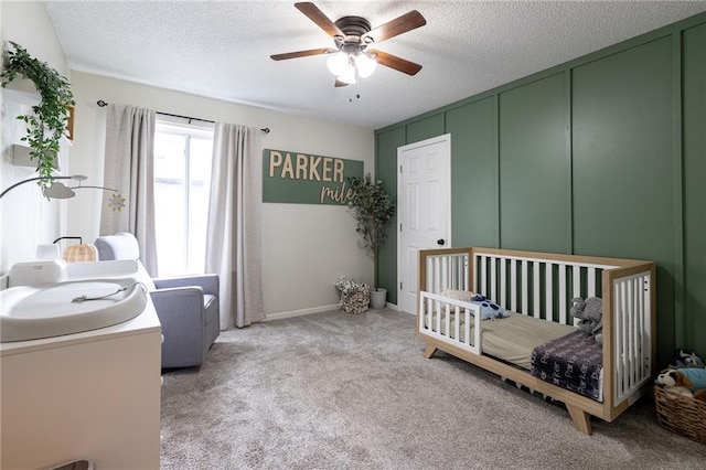 carpeted bedroom with a nursery area, a ceiling fan, and a textured ceiling