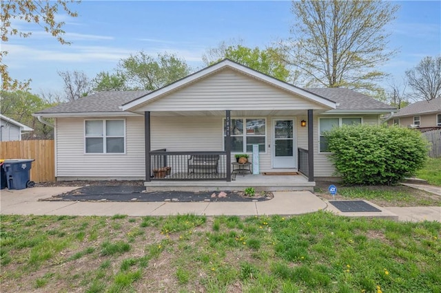exterior space with covered porch, roof with shingles, a front lawn, and fence