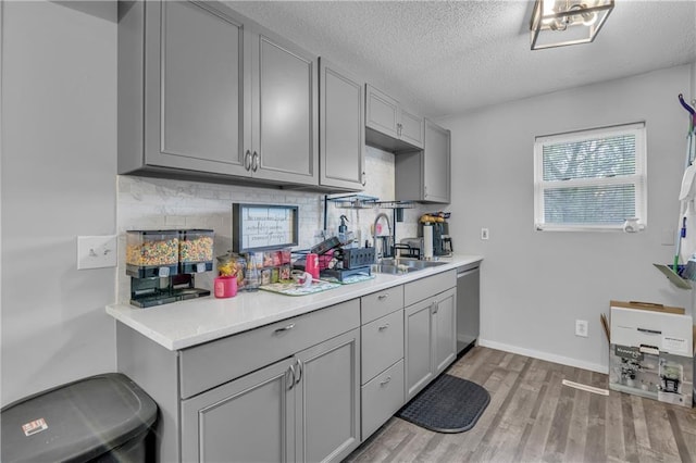 kitchen featuring light wood-type flooring, stainless steel dishwasher, decorative backsplash, and gray cabinetry
