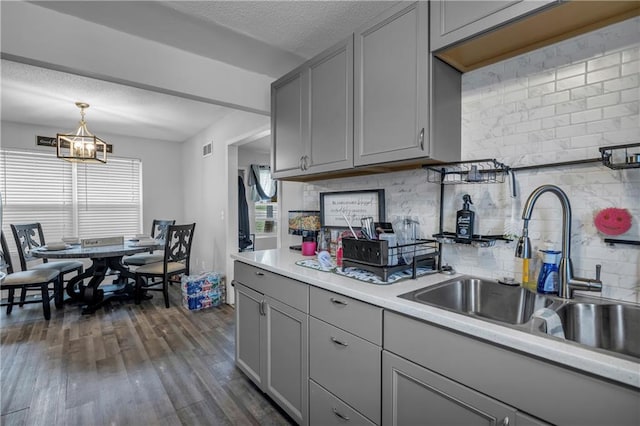kitchen featuring a sink, a notable chandelier, decorative backsplash, gray cabinetry, and light countertops