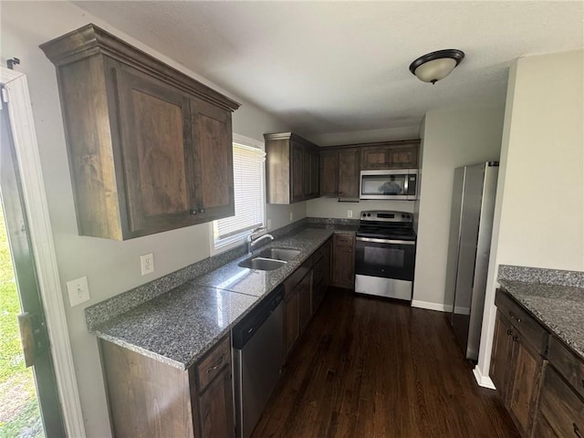 kitchen featuring stainless steel appliances, a sink, dark brown cabinets, baseboards, and dark wood-type flooring