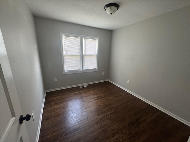 unfurnished room featuring baseboards, visible vents, and dark wood-style floors