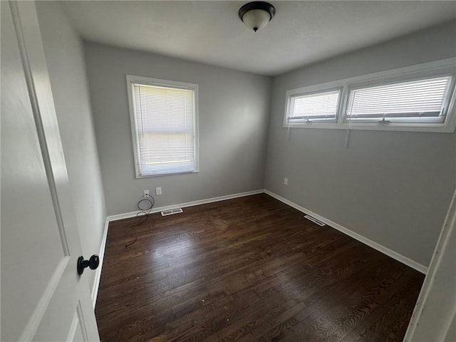 spare room featuring baseboards, visible vents, and dark wood-type flooring