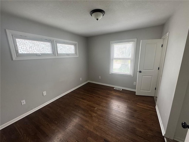 unfurnished room with baseboards, visible vents, a textured ceiling, and dark wood-style floors