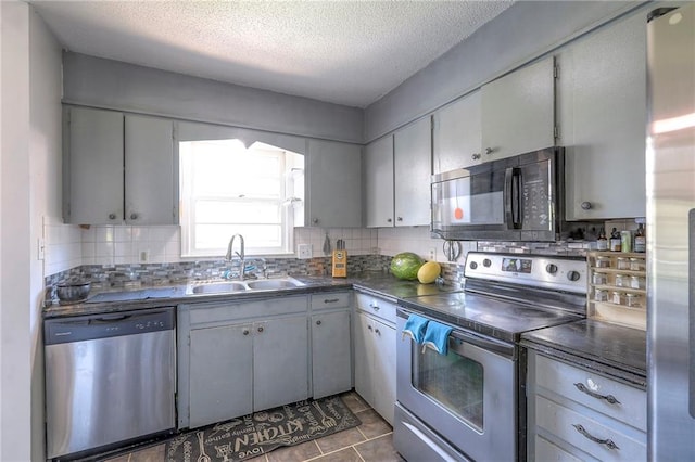 6606 E 135th St, Grandview, MO 64030 - kitchen with stainless steel appliances, a sink, dark countertops, decorative backsplash, and a textured ceiling
