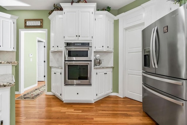 5720 NE Quartz Dr, Lees Summit, MO 64064 - kitchen with decorative backsplash, light wood finished floors, white cabinets, and stainless steel appliances