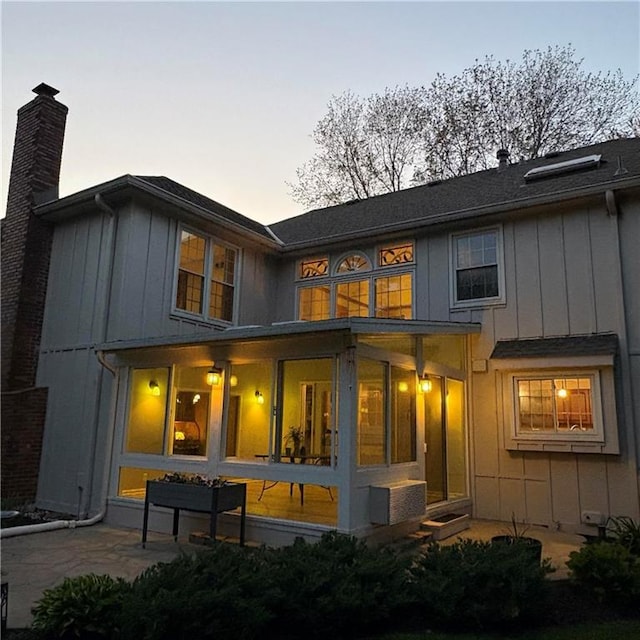 2405 W 123rd Ter, Leawood, KS 66209 - back of property at dusk with a chimney, a sunroom, a patio area, and board and batten siding