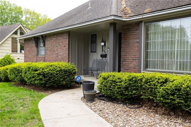 view of exterior entry with brick siding, board and batten siding, and roof with shingles
