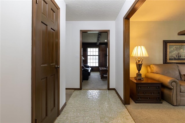 hall with a textured ceiling, baseboards, and light colored carpet