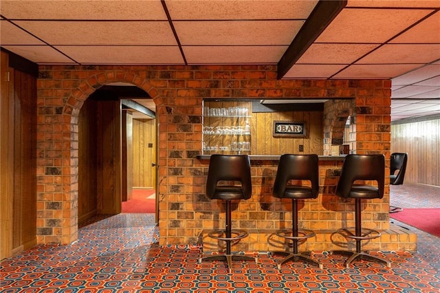 bar featuring wooden walls, arched walkways, a bar, and a paneled ceiling