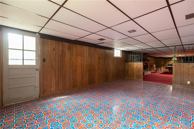 basement featuring a drop ceiling and wooden walls