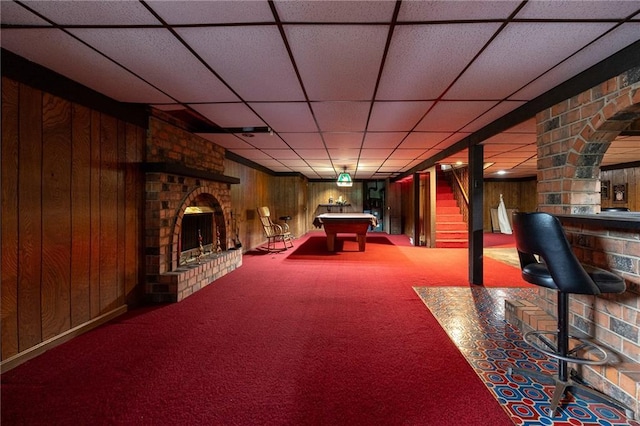 playroom with billiards, a fireplace, carpet floors, wooden walls, and a drop ceiling