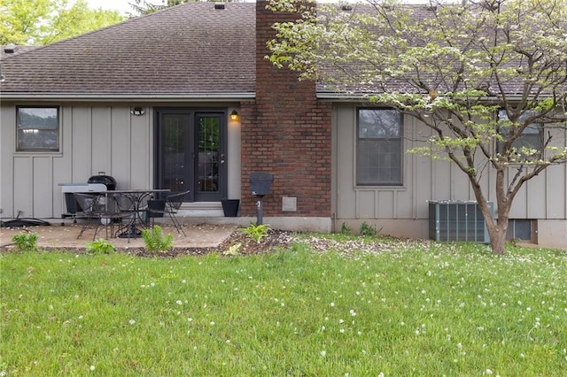 rear view of house with board and batten siding, a patio, roof with shingles, and a lawn