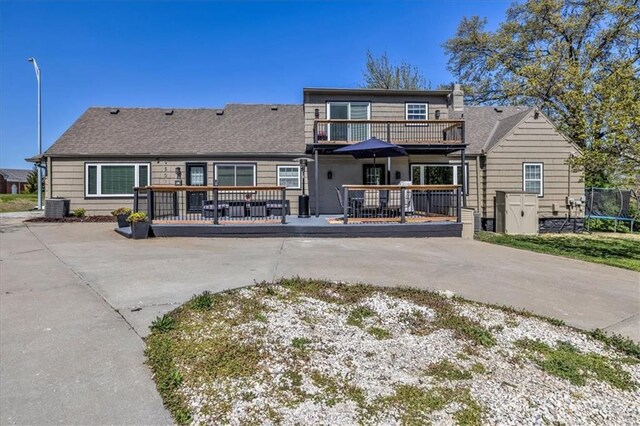 9501 Wornall Rd, Kansas City, MO 64114 - rear view of house featuring a deck, a balcony, central air condition unit, roof with shingles, and a trampoline