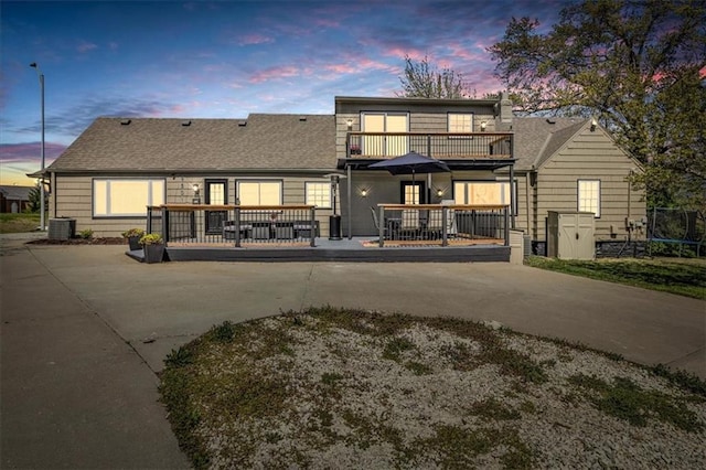 9501 Wornall Rd, Kansas City, MO 64114 - back of house at dusk featuring a shingled roof, driveway, a balcony, and central AC