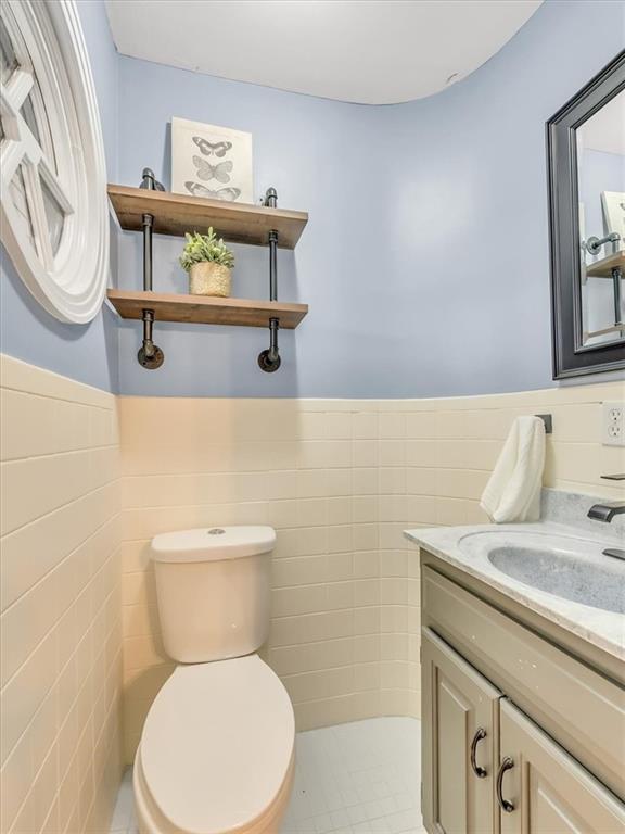 9501 Wornall Rd, Kansas City, MO 64114 - half bath featuring tile walls, toilet, vanity, and a wainscoted wall