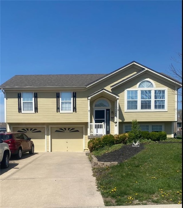raised ranch with an attached garage, driveway, and a front lawn