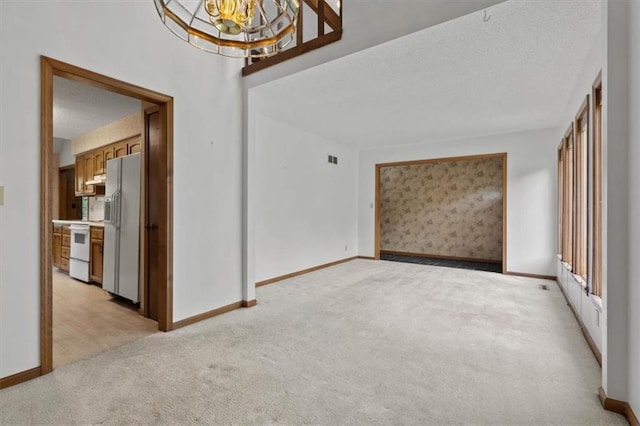 empty room with a textured ceiling, baseboards, light colored carpet, and an inviting chandelier