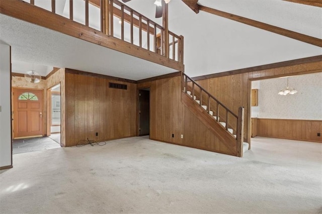 unfurnished living room featuring visible vents, wood walls, stairway, high vaulted ceiling, and carpet flooring