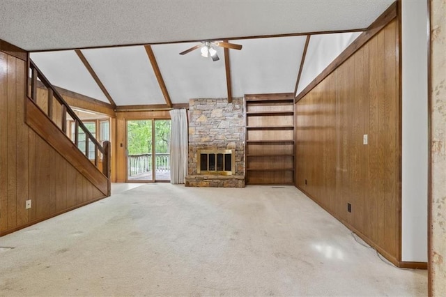 unfurnished living room with wood walls, stairs, vaulted ceiling with beams, a ceiling fan, and carpet