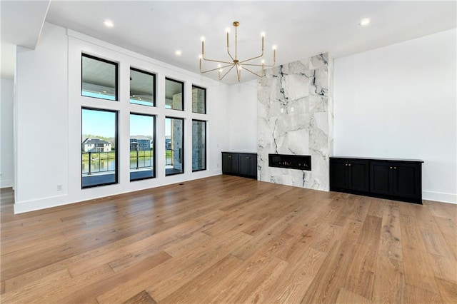 unfurnished living room with a fireplace, an inviting chandelier, light wood finished floors, and recessed lighting