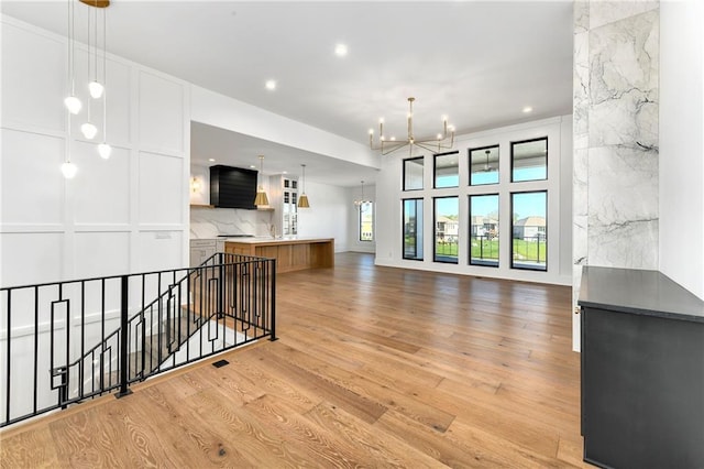 unfurnished living room with light wood finished floors, a sink, recessed lighting, and a chandelier