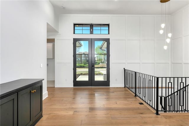 foyer featuring light wood-style flooring, a decorative wall, baseboards, and french doors