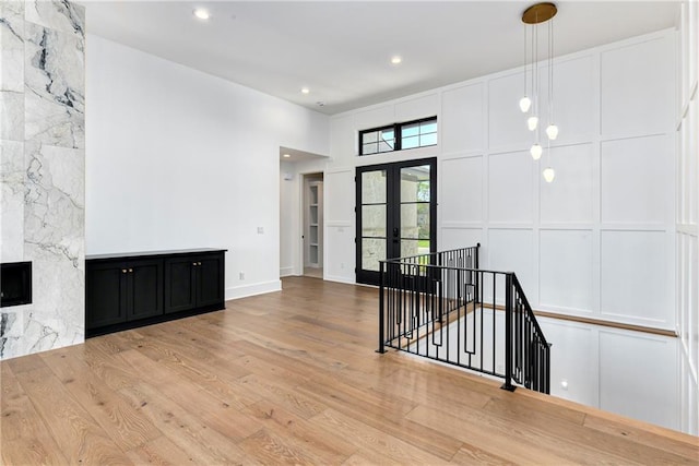 interior space with wood finished floors, french doors, a large fireplace, baseboards, and recessed lighting