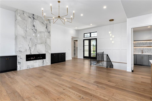 unfurnished living room with a high end fireplace, an inviting chandelier, wood finished floors, and recessed lighting