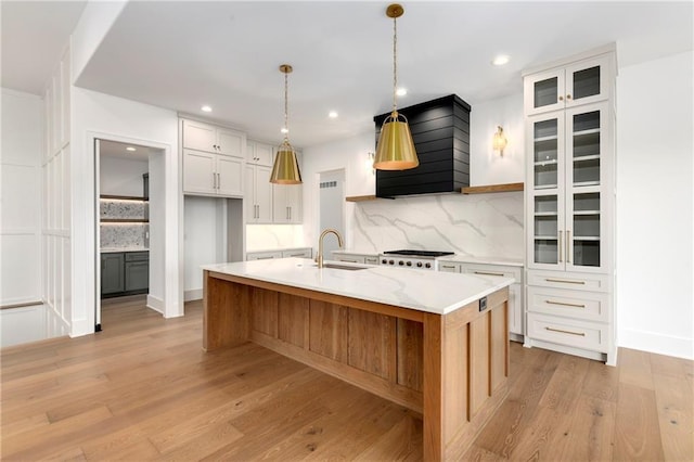 kitchen with decorative backsplash, light wood-style flooring, a sink, and custom range hood
