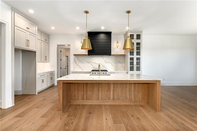kitchen with a sink, light wood finished floors, premium range hood, backsplash, and recessed lighting