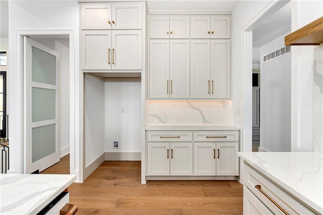 kitchen with light stone counters, light wood-style floors, backsplash, and white cabinetry