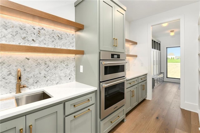 kitchen with double oven, open shelves, light countertops, a sink, and decorative backsplash