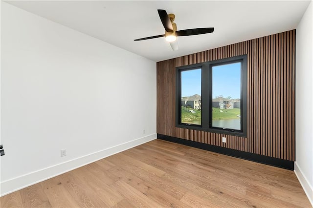 spare room featuring light wood-type flooring, a ceiling fan, and baseboards