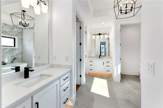 full bath with two vanities, a sink, a notable chandelier, and toilet
