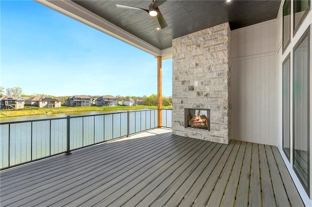 wooden deck featuring ceiling fan, an outdoor stone fireplace, a residential view, and a water view