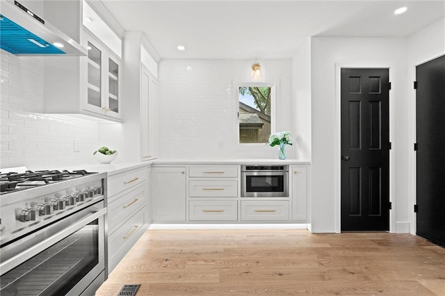 224 NW Locust St, Lees Summit, MO 64064 - kitchen with stainless steel appliances, range hood, white cabinets, backsplash, and light wood finished floors
