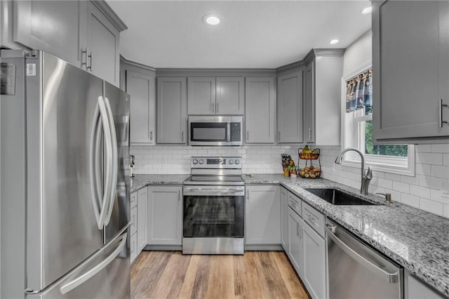 kitchen with appliances with stainless steel finishes, a sink, gray cabinets, light stone counters, and recessed lighting
