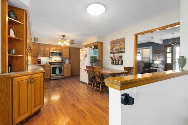 108 Sunrise Ct, Ozawkie, KS 66070 - kitchen with open shelves, wood finished floors, brown cabinetry, ceiling fan, and appliances with stainless steel finishes