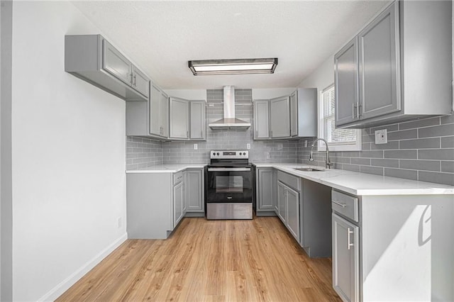 kitchen with light wood finished floors, a sink, stainless steel electric range, gray cabinets, and wall chimney range hood