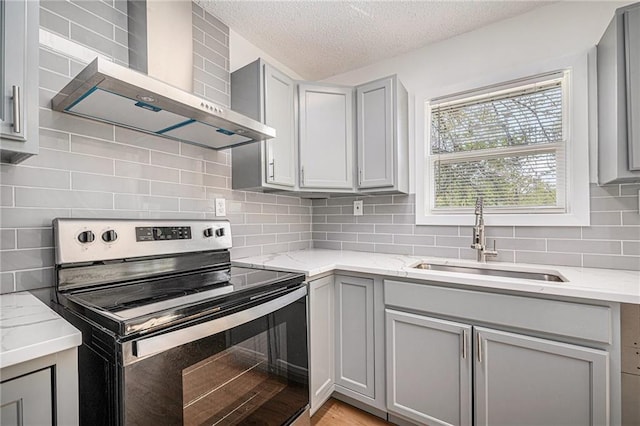kitchen with a sink, stainless steel electric range, gray cabinets, wall chimney range hood, and a textured ceiling