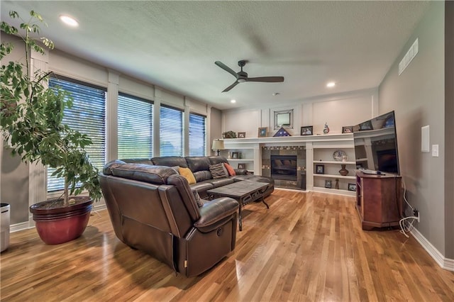 living room with visible vents, a ceiling fan, wood finished floors, and a tile fireplace